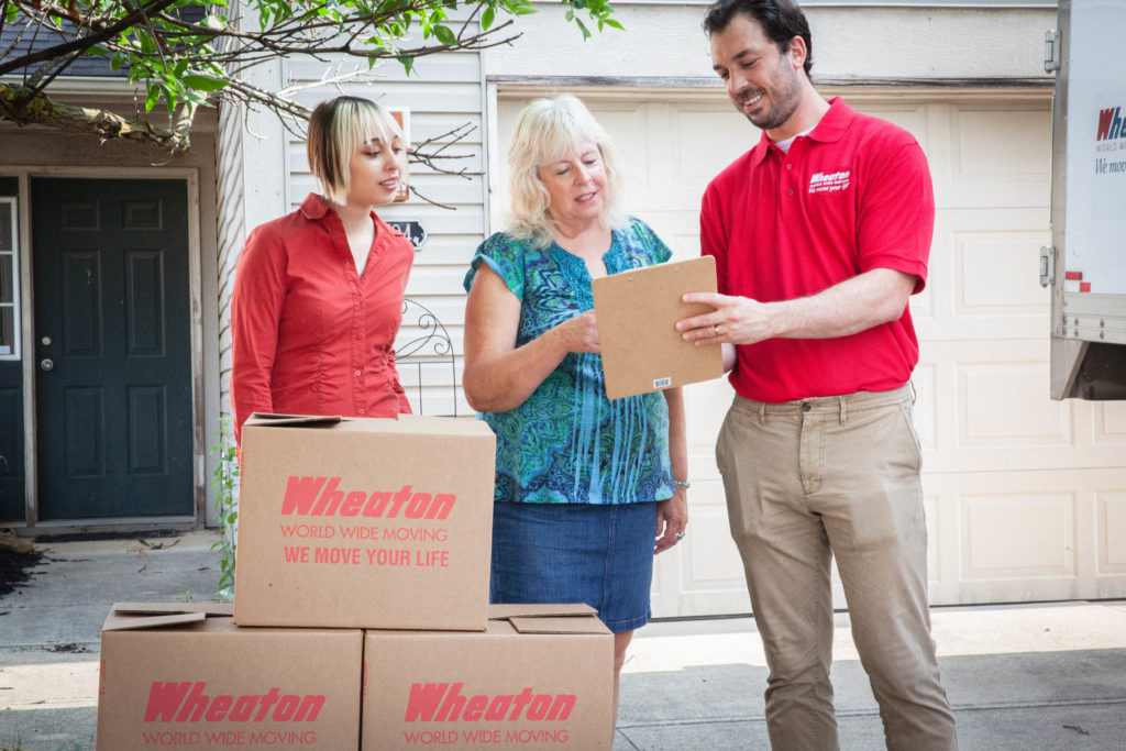 A mover from Wheaton World Wide Moving signing a contract with two women.