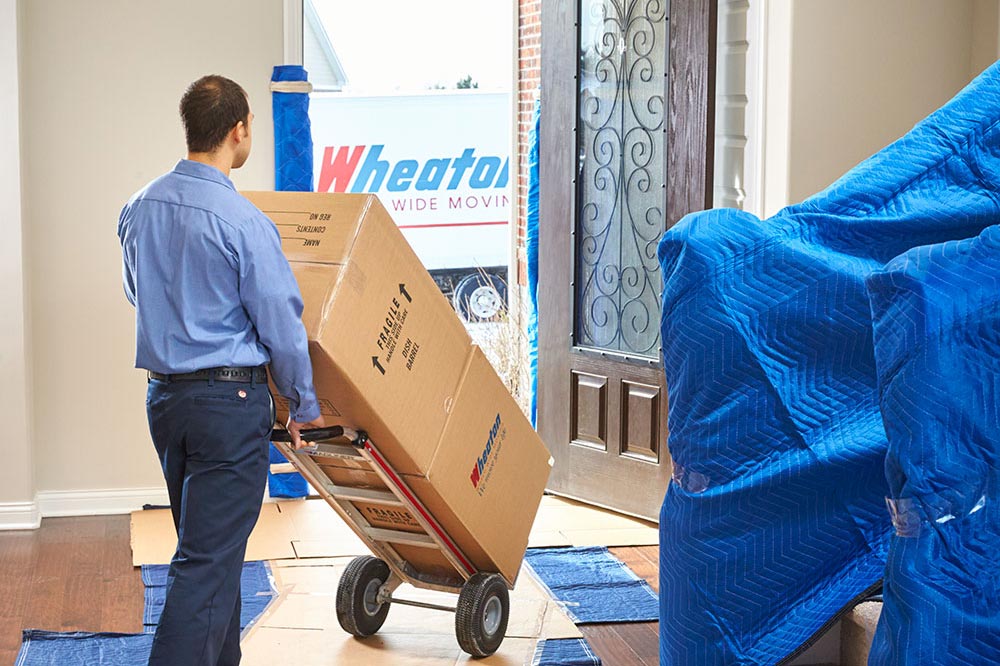 A mover rolling two boxes out of a home on a dolly
