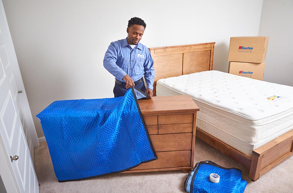 A mover wrapping a dresser with a moving blanket