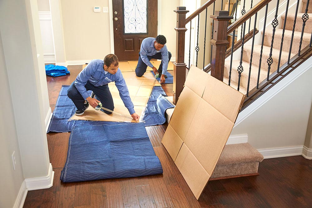 Two movers from Wheaton Worldwide Moving wrapping cardboard boxes with moving blankets
