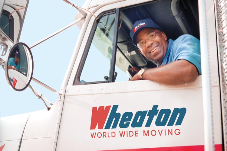 A smiling driver leaning out the window of a Wheaton Worldwide Moving truck