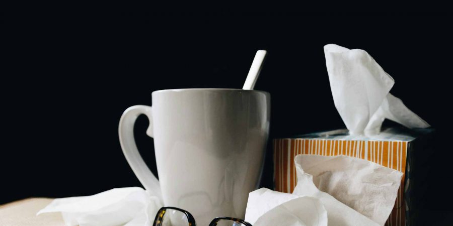 A mug of tea and a pair of glasses, sitting on a table with some crumpled up tissues
