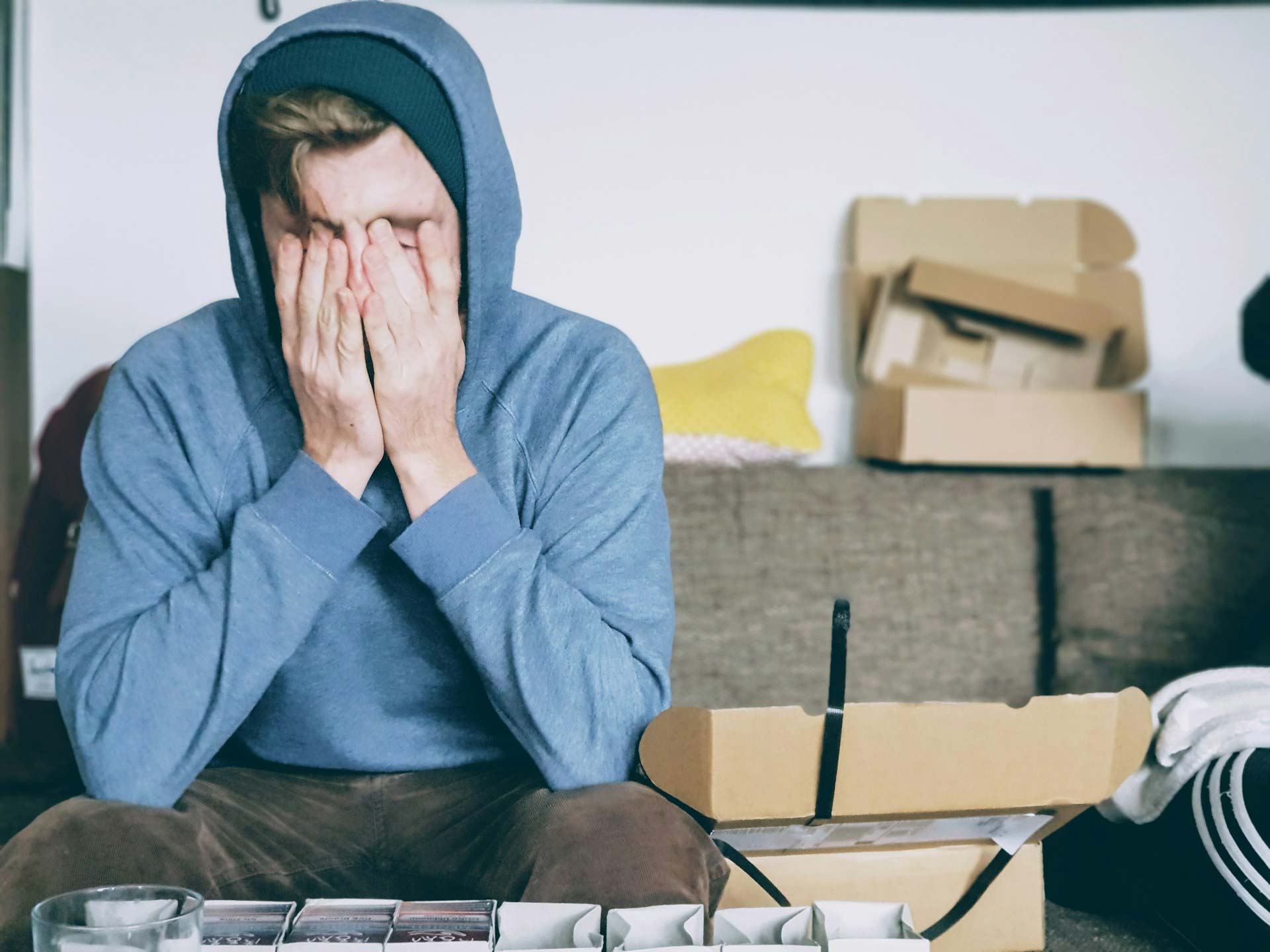 Visibly stressed man with head in his hands, on couch surrounded by boxes