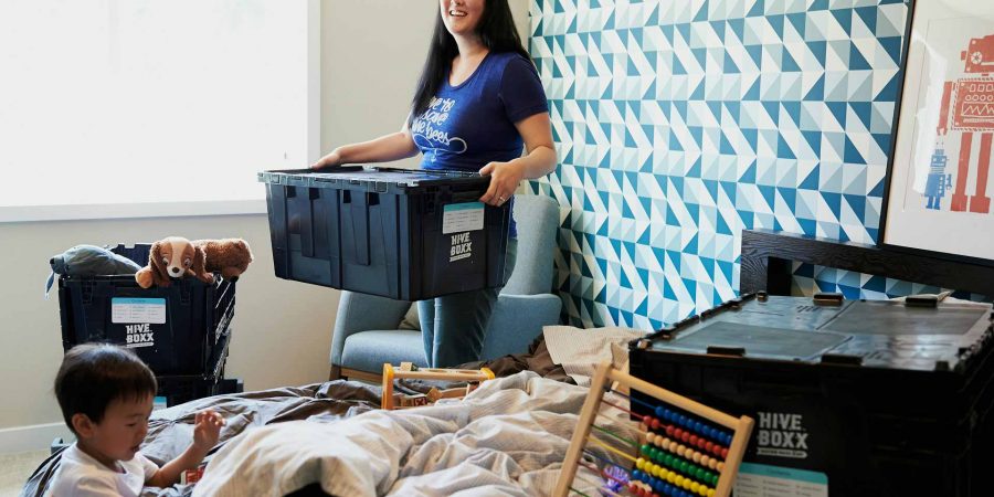 Woman packing child's toys up in to several black storage boxes