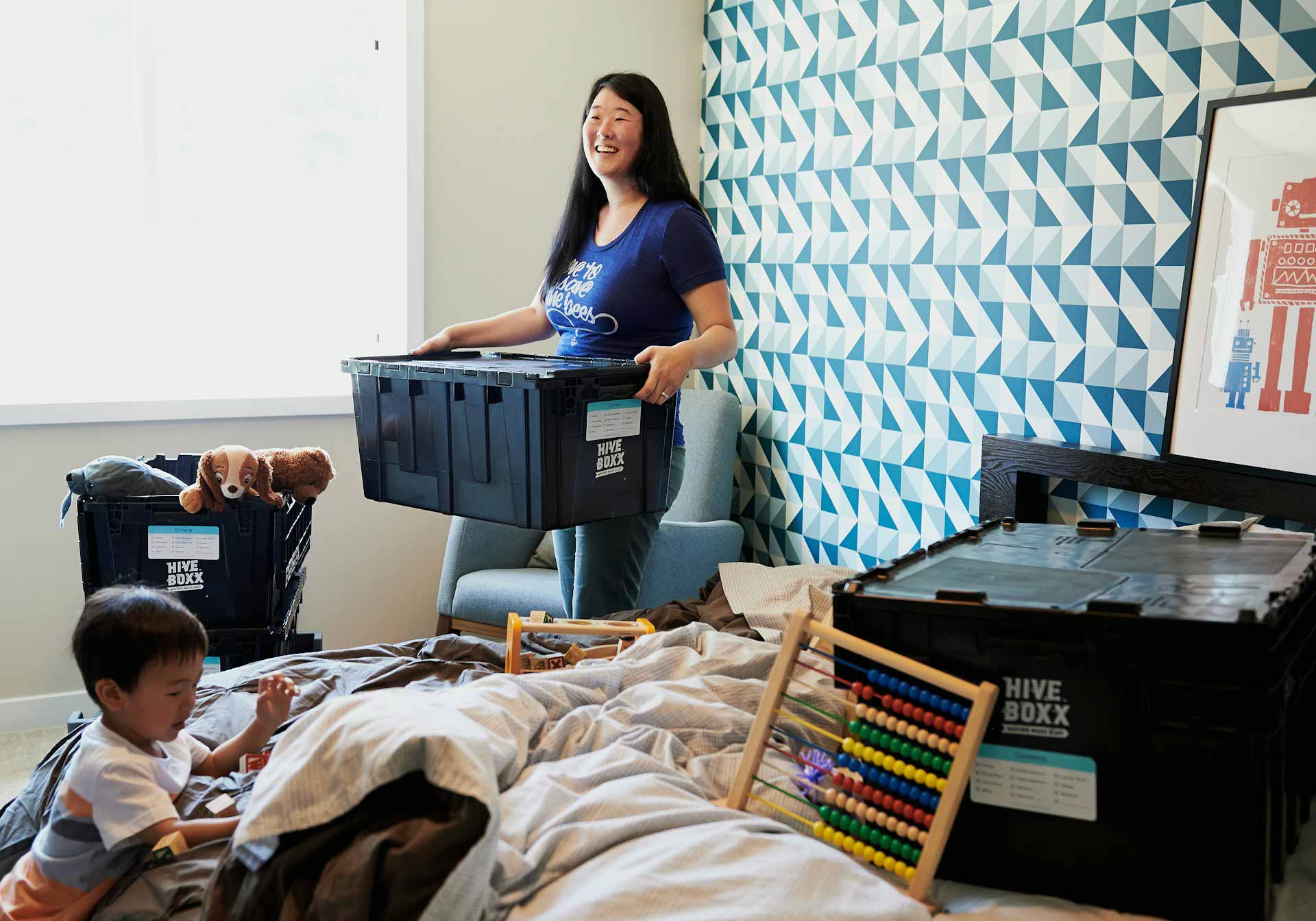Woman packing child's toys up in to several black storage boxes