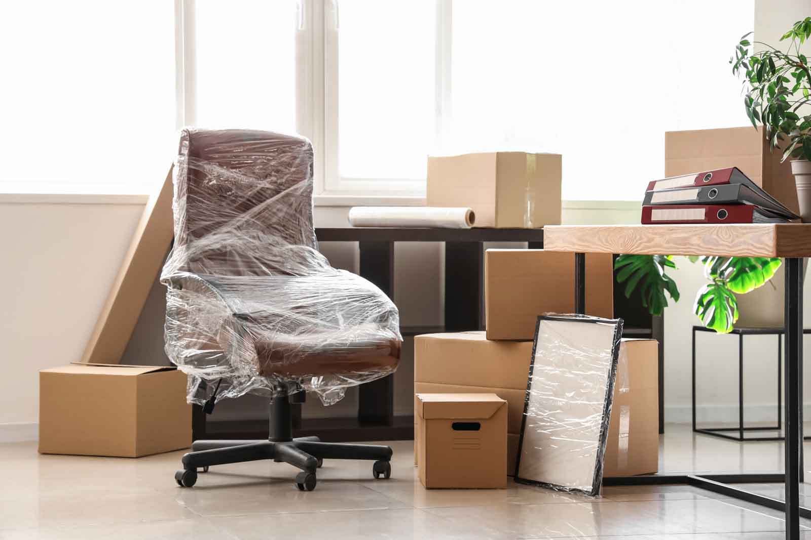 Moving boxes stacked in office space. A desk chair is wrapped in plastic